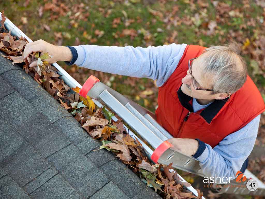 man outside on a ladder cleaning leaves out of gutters