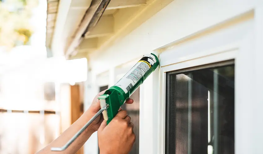 Person Caulking the trim of their window on the exterior of their house.